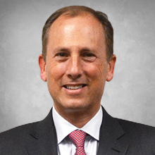 Man in black suite with white shirt and red tie headshot