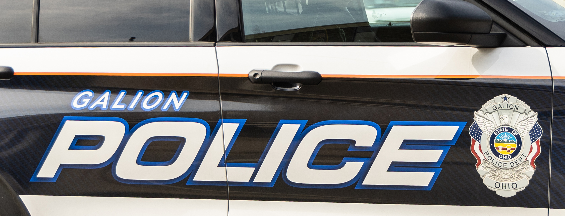 white police car with small orange stipe and big black stripe with white text that has blue outline and a police badge on the right-hand side