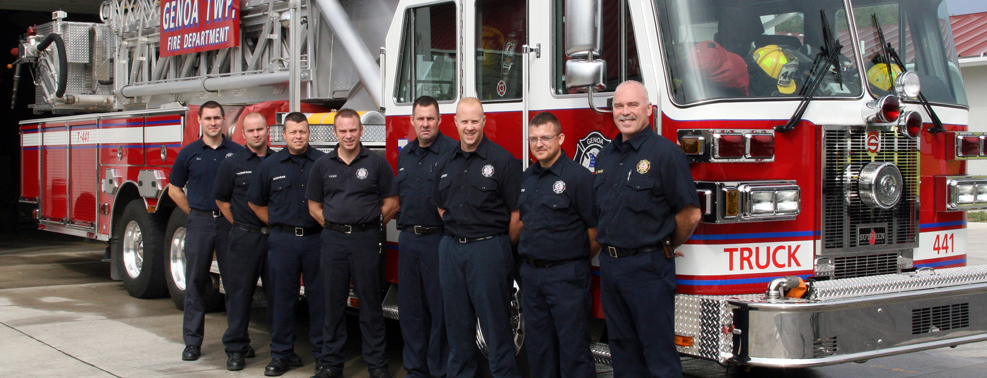 eight firefighters standing in a line next to a red and white firetruck 