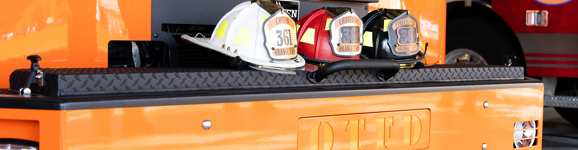 one black, one red and one white fire helmet sitting on the front bumper of an orange fire truck