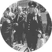 Black and white image of a police officer standing next to a child and a marching drum 