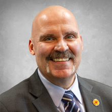 bald man with mustache wearing a grey suite with tie headshot