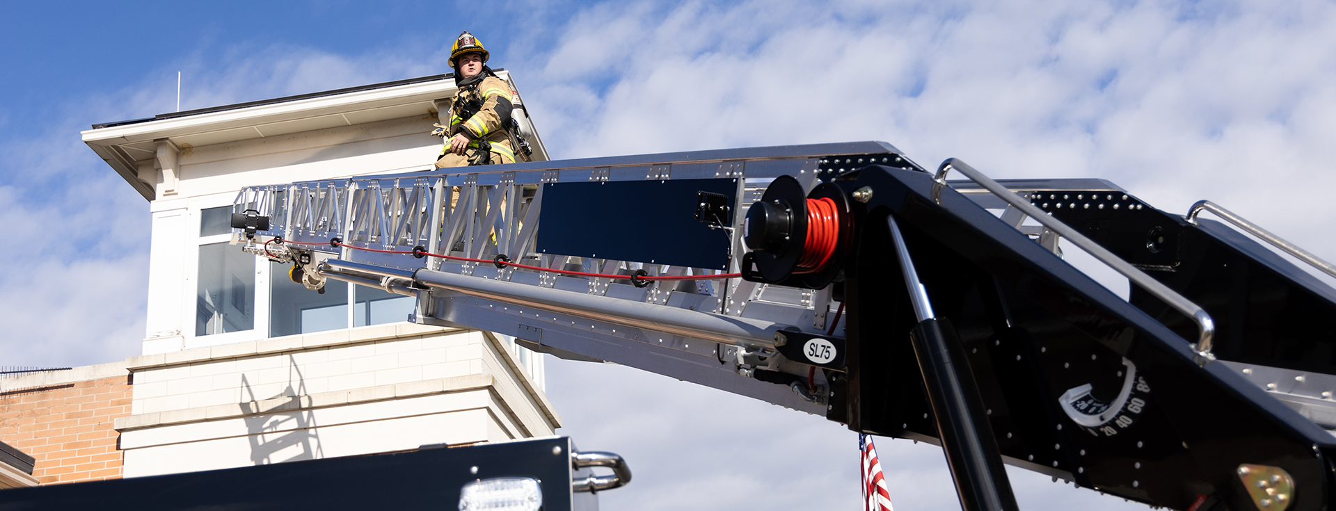 firefighter climbing on a ladder towards a building with a cloudy sky 