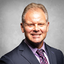 board member headshot in blue suite with purple shirt and tie