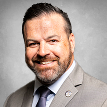 man with a beard in grey suite with blue shirt and dark purple tie 