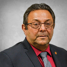 Man with glasses in black suite with a red shirt and grey tie headshot